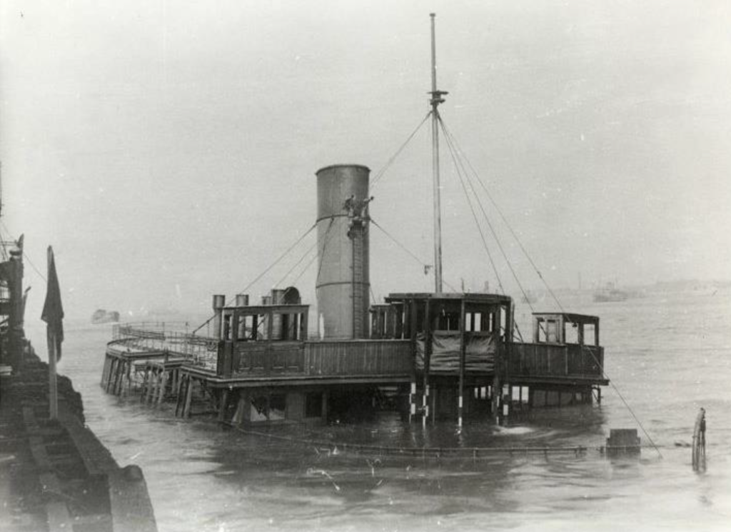 An old black and white photograph of a ferry boat submerged up to her upper decks in the water.